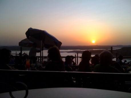 The sun sets over Lake Travis as people at The Oasis Restaurant watch